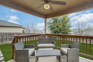 Relax in this serene outdoor space with a ceiling fan overhead, wicker furniture, and a beautiful lawn view.