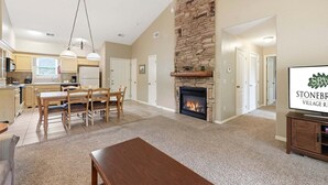 A spacious living area with a fireplace, dining table, and kitchen in the background. - Condo & Queen Suite at StoneBridge (Reeds Spring)
