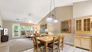 A dining area with a wooden table and chairs, a chandelier, and a kitchen with wooden cabinets. - Condo & Queen Suite at StoneBridge (Reeds Spring)