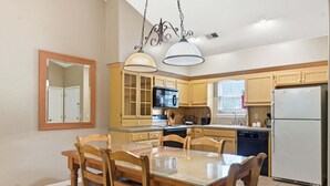 A kitchen with wooden cabinets, a dining table with chairs, a microwave, a refrigerator, and pendant lights. - Condo & Queen Suite at StoneBridge (Reeds Spring)