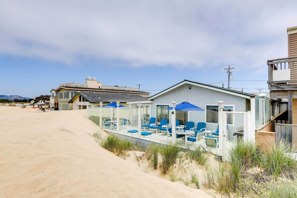 Een strandpand met een overdekte patio, inclusief buitenmeubilair en parasols.