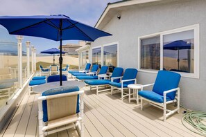 Een terras met blauwe ligstoelen en een tafel, witte relingen en uitzicht op het strand.