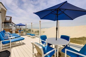 Een terras met blauwe en witte lounge stoelen, een ronde tafel en een grote blauwe parasol.