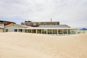 Een modern gebouw met een plat dak en grote ramen, omgeven door duinen.