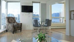 A modern living room with a patterned armchair, a glass coffee table, and a dining area with chairs.
