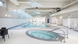 A large indoor swimming pool with a central diving area, surrounded by seating and a high ceiling with visible ductwork.