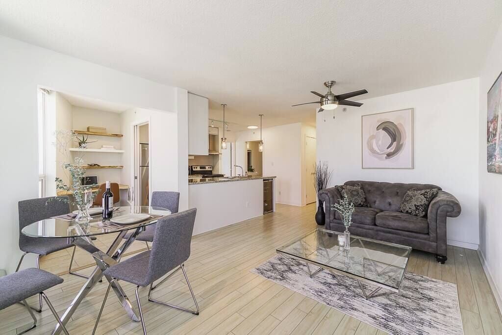Un salon moderne avec une table basse en verre, des canapés gris et un coin repas comprenant une table et des chaises en verre.