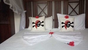A neatly made bed with a white bedspread, two pillows with skull and crossbones designs, and a red flower decoration.