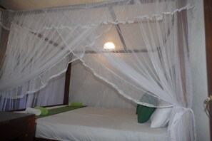 A single bed with a white bedspread, a green pillow, and a green blanket.