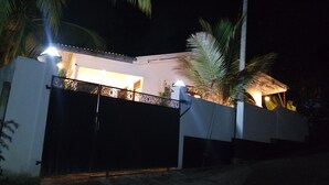 A modern house with a gated entrance, a covered patio area, and a well-lit exterior at night.