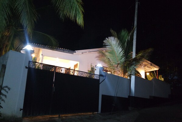 A modern house with a gated entrance, a covered patio area, and a well-lit exterior at night.