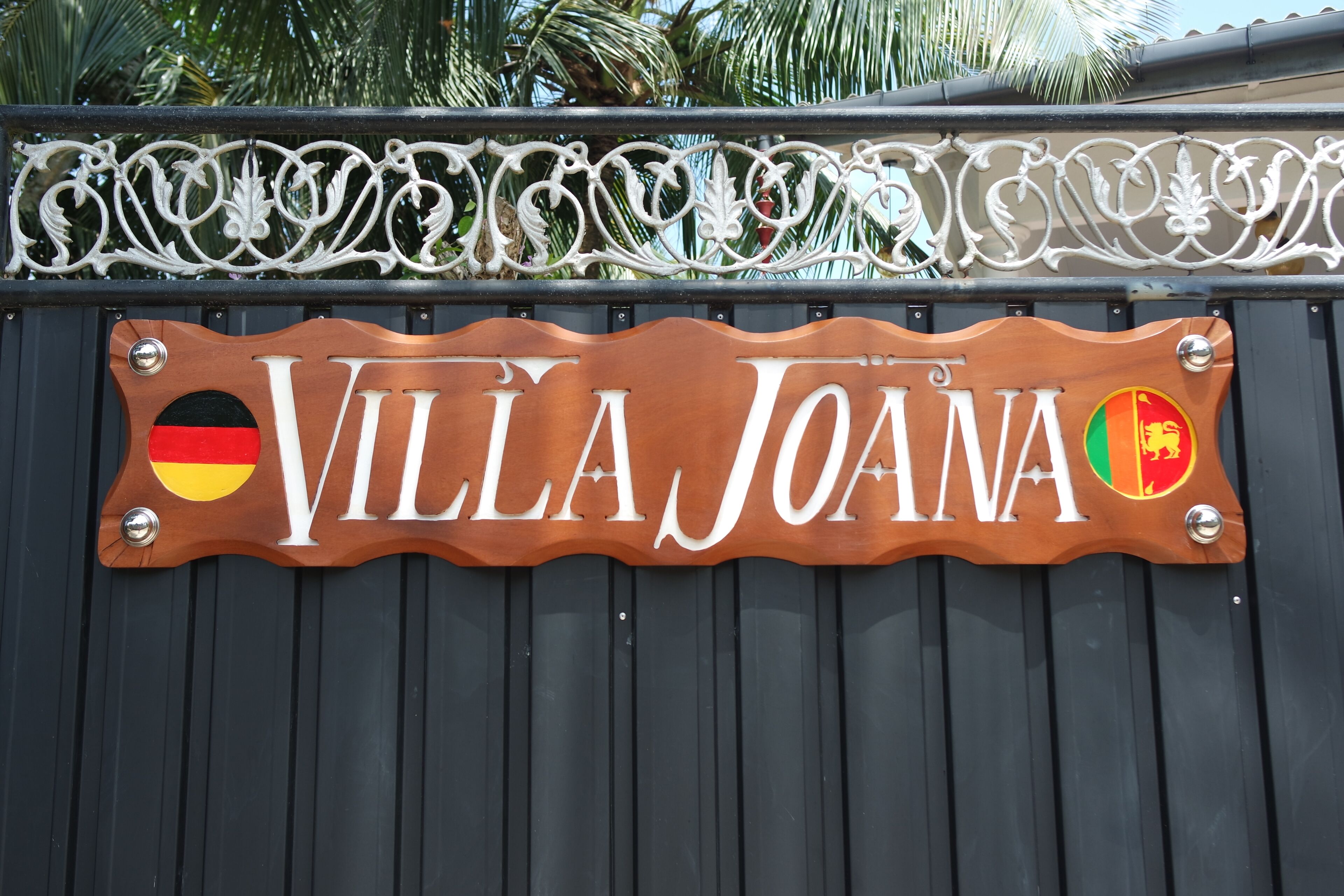 Une enseigne en bois portant le nom « VILLA JOANA » et deux drapeaux.