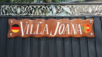 Une enseigne en bois portant le nom « VILLA JOANA » et deux drapeaux.