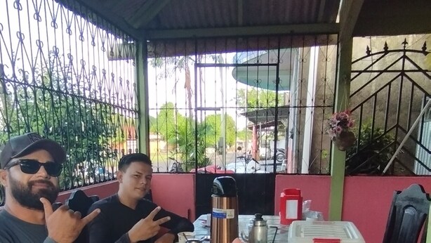 Un área de comedor al aire libre con techo, con una mesa lista para dos personas, mostrando una variedad de platillos y bebidas.