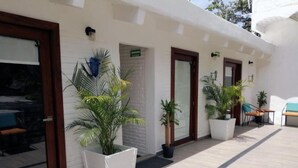 A building with a white exterior, large potted plants, and a tiled patio area with outdoor seating.