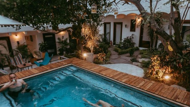 A swimming pool with wooden deck, surrounded by potted plants and outdoor furniture.