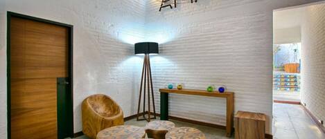 Un interior moderno con pared de ladrillo blanco, una puerta de madera, una lámpara de pie y una mesa pequeña con objetos decorativos.