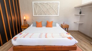 Un lit bien fait, avec une couette blanche et des oreillers orange, une lampe de chevet et une œuvre d’art abstraite accrochée au mur.