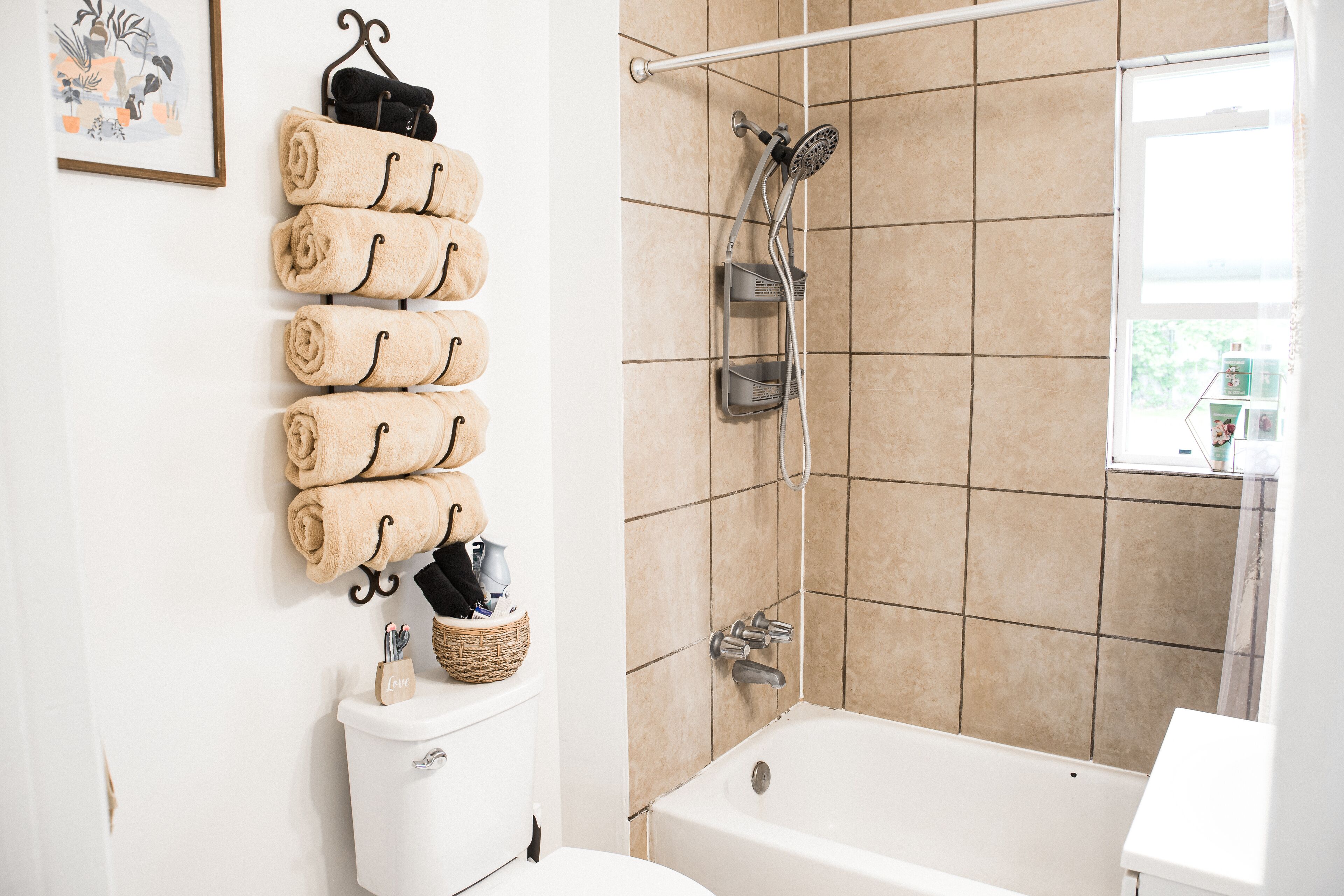 A bathroom with a toilet, a bathtub, and a shower. There are towels hanging on a rack and a basket with toiletries.