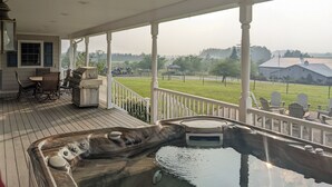 Une terrasse extérieure couverte, dotée d’un jacuzzi, d’un espace salon et offrant une vue sur un paysage rural.