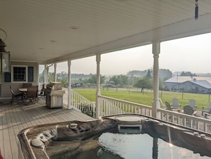 Relax in a serene outdoor space with a hot tub and comfortable seating, overlooking a lush green field and distant buildings.