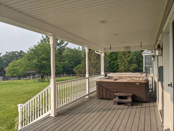 A covered wooden deck with a hot tub, white railings, and a view of a grassy yard and trees. - Perfect View: Plenty of room for everyone to stay and play! (Davis)