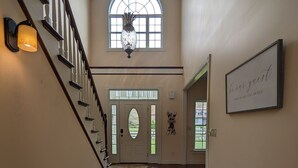Un hall d’entrée spacieux avec un plancher en bois, un escalier doté d’une rampe blanche, une grande fenêtre en arc de cercle et une pancarte de bienvenue.