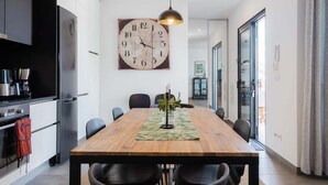 A modern kitchen with a wooden dining table, black chairs, and a large wall clock. - GuestReady - Anakaj House (Funchal)