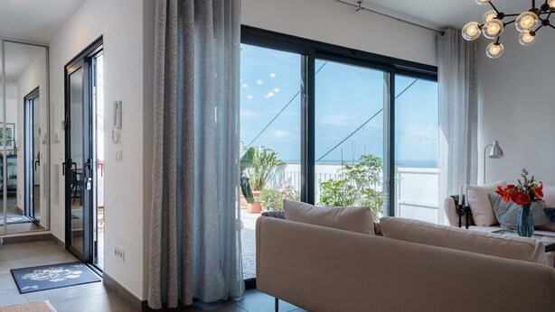 A modern living room with a sofa, a coffee table, and a view of the outdoors through large windows. - GuestReady - Anakaj House (Funchal)
