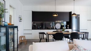 A modern kitchen with black cabinets, a dining area with a wooden table and black chairs, and a white sofa with floral cushions. - GuestReady - Anakaj House (Funchal)