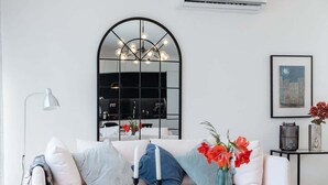 A modern living room with a white sofa, a glass coffee table, a vase with flowers, a black-framed mirror, and a framed picture on the wall. - GuestReady - Anakaj House (Funchal)