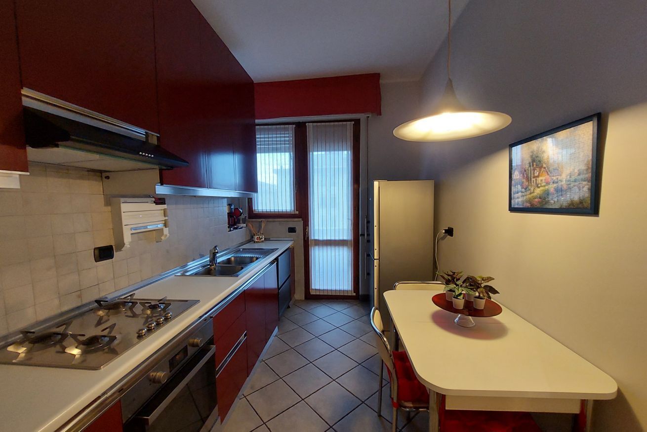 A compact kitchen with a stove, sink, and cabinets, a dining area with a table and chairs, and a window with blinds.
