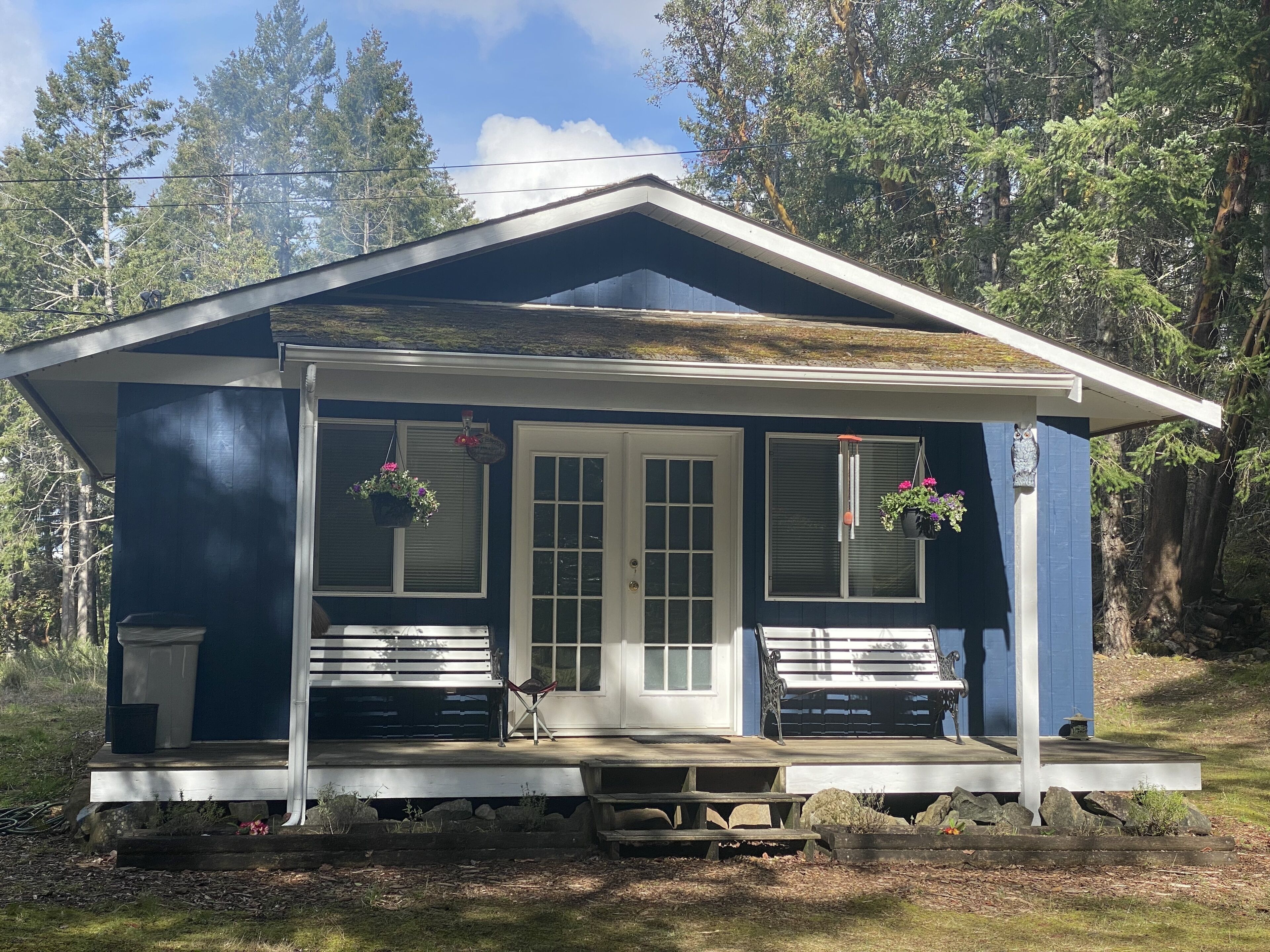 Een klein, gelijkvloers vakantiehuisje met een veranda, twee bankjes en bloembakken.