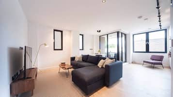 A modern living room with a sectional sofa, a flat-screen TV, and a large window providing natural light.