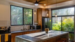 A modern kitchen with large windows, wooden cabinets, and a central island with stools.