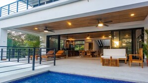 A modern outdoor pool area with a wooden deck, lounge chairs, and a dining area.