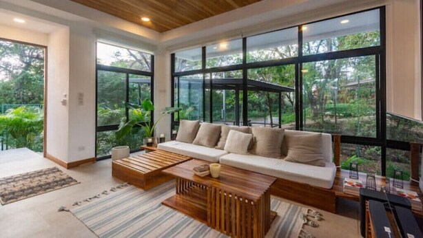A modern living room with a large window, a wooden ceiling, and a sofa with cushions.