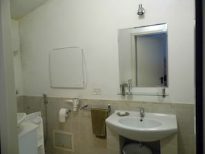 A bathroom with a sink, mirror, towel rack, and toilet paper.