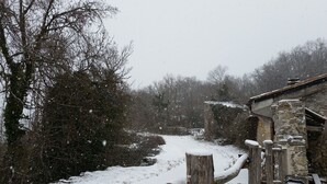 Ein verschneiter Pfad führt zu einem Steinhaus mit Holzzaun.