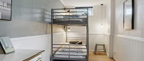 A bunk bed room with a dresser, a small stool, and a framed picture on the wall.