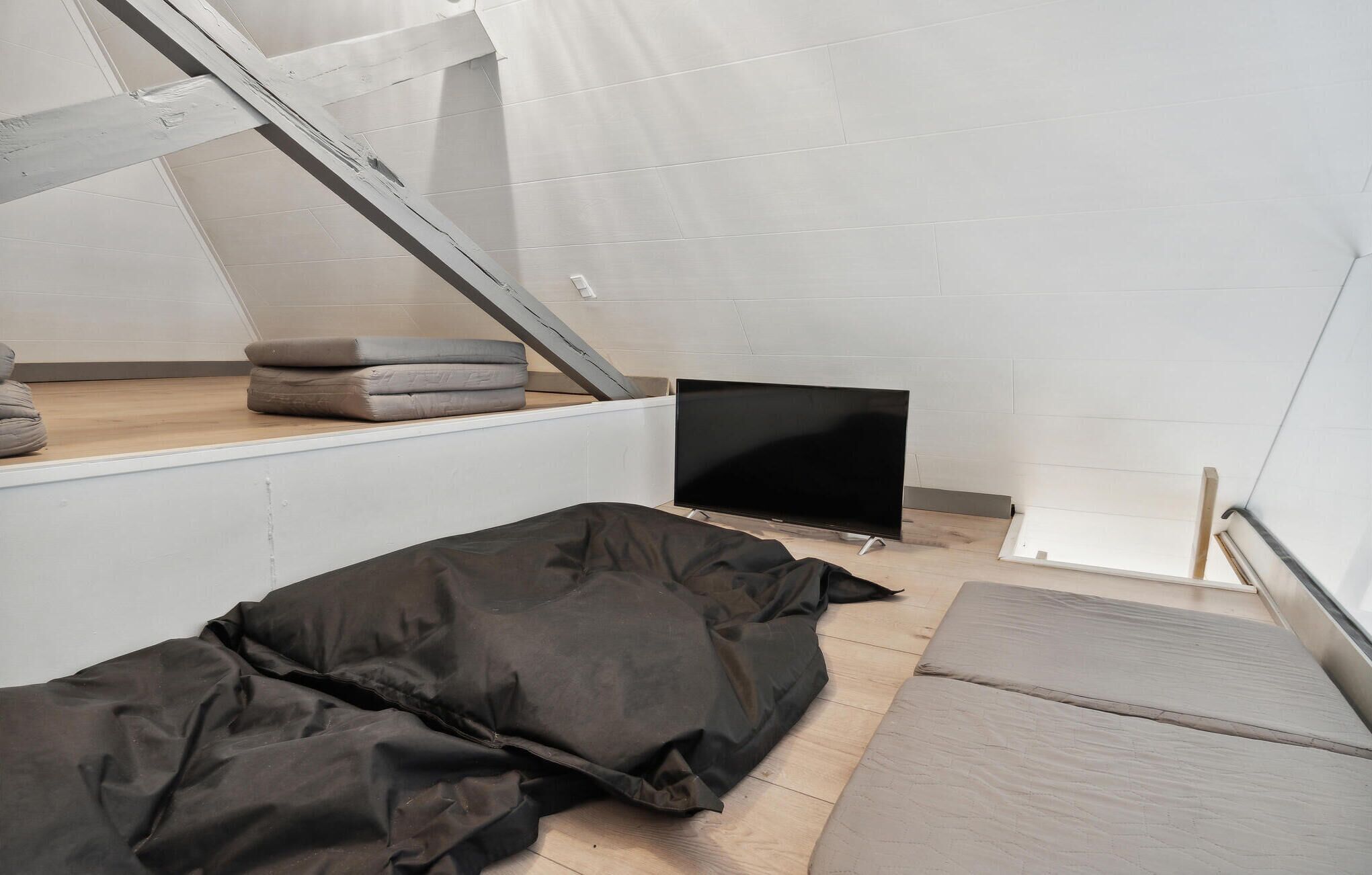 Una habitación compacta y moderna con techo inclinado, televisor de pantalla plana y cama con colchón gris.