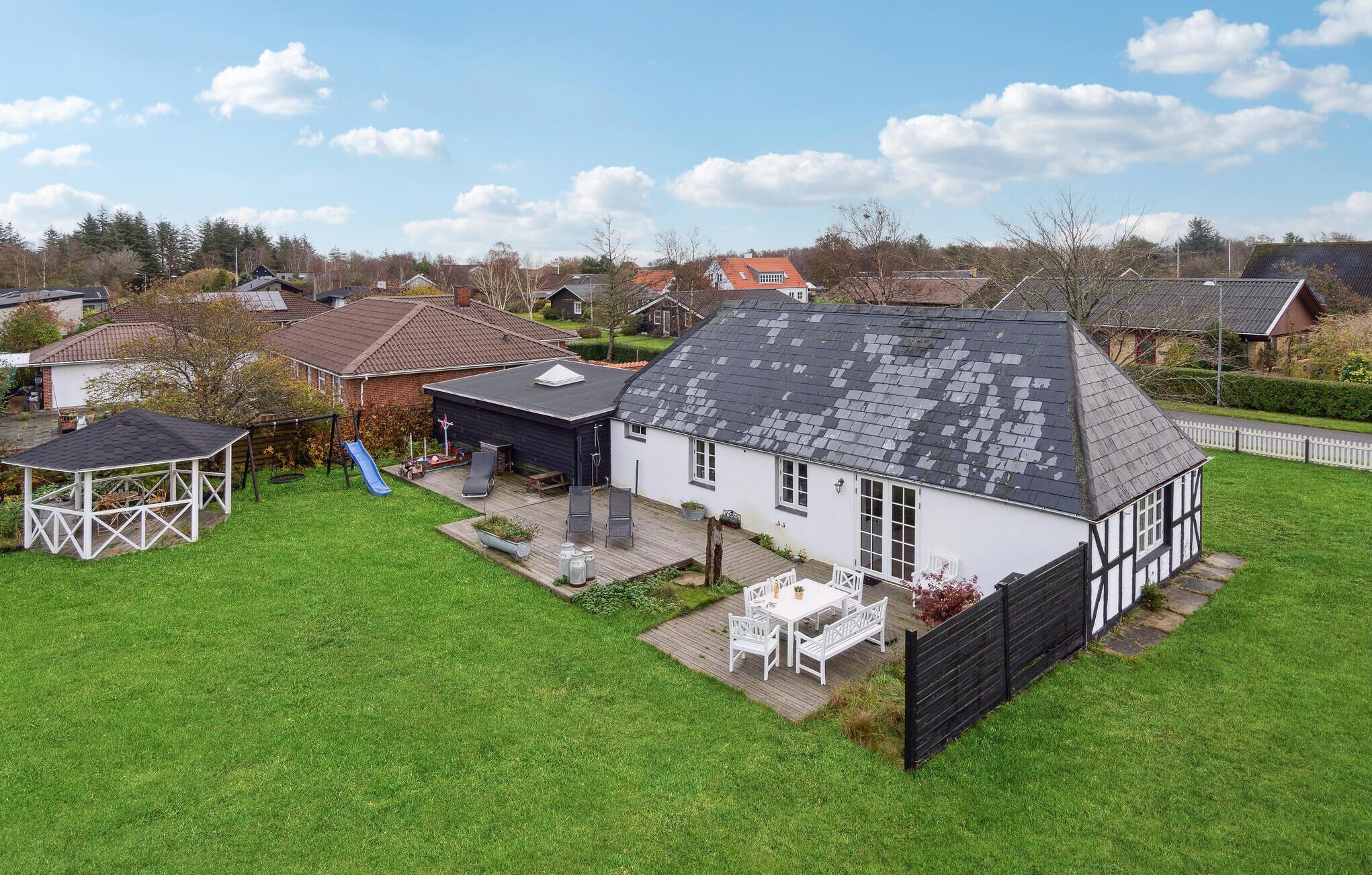 Een huis met een ruime achtertuin, een overdekt terras en een witte hek.