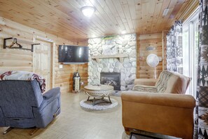 A cozy cabin interior with a stone fireplace, wooden walls, a flat-screen TV, and a comfortable seating area. - Lakefront Phelps Cabin w/ Boat Dock & Water Toys! (Phelps)