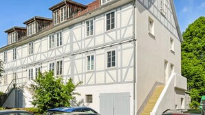 Un immeuble à plusieurs étages doté d’une façade traditionnelle à colombages, d’un escalier apparent et d’une voiture garée au premier plan.