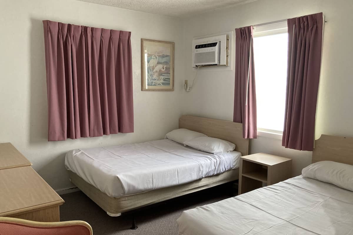 A hotel room with a single bed, a bedside table, a chair, and a window with curtains.