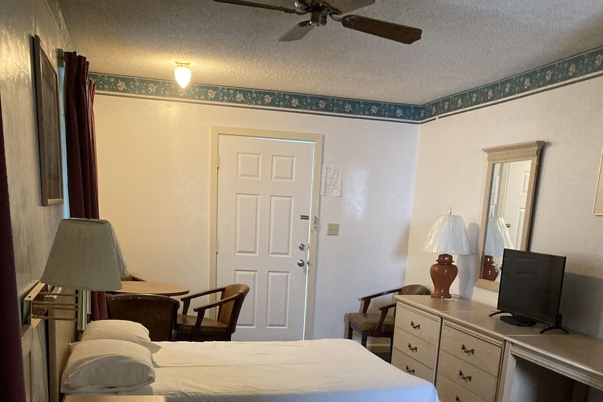 A hotel room with two beds, a desk with a computer, a chair, a lamp, and a ceiling fan.