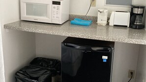 Uma cozinha compacta equipada com micro-ondas, torradeira, cafeteira e um cesto de lixo.