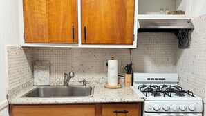 Une cuisine avec des meubles en bois, un plan de travail en granit, un évier en acier inoxydable, une cuisinière à gaz et un four blanc.
