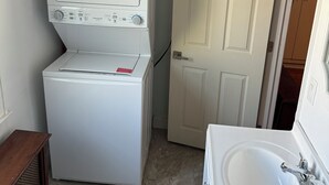 A compact laundry room with a front-loading washer and dryer, a white door, and a sink with a mirror. - Spring Lake Retreat ~ Extended Monthly Stays - New York City Access (South Plainfield)