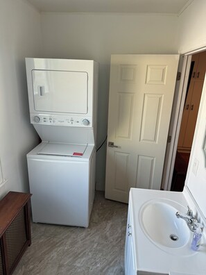 A compact laundry room with a front-loading washer and dryer, a white door, and a sink with a mirror. - Spring Lake Retreat ~ Extended Monthly Stays - New York City Access (South Plainfield)